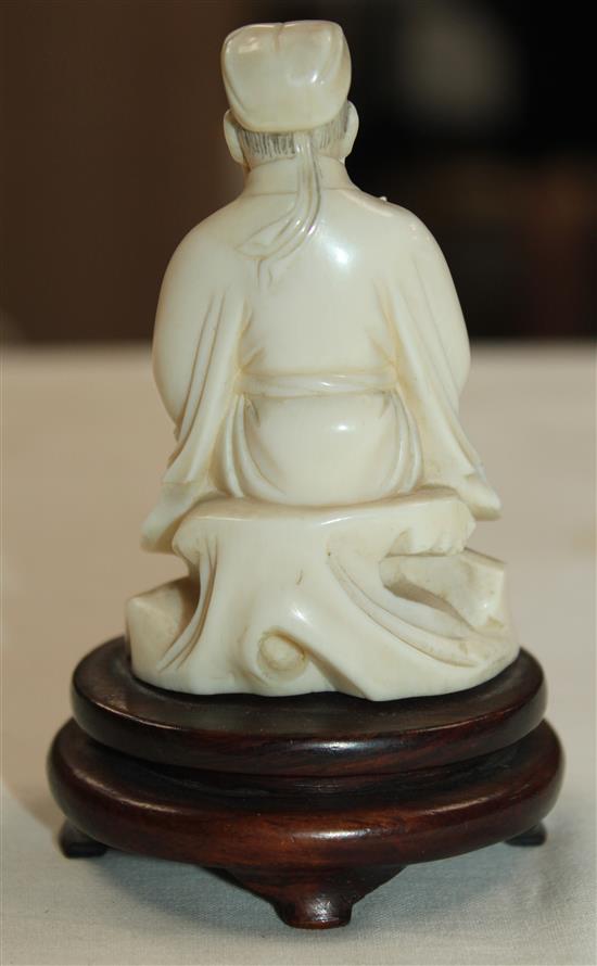 A Chinese ivory seated figure of a scholar holding a bird, early 20th century, wood stand, total height, 10cm